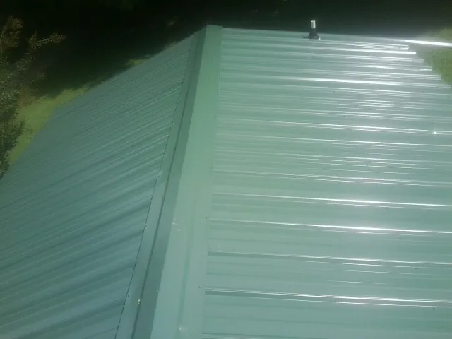 New green metal panels meeting at the ridge of a roof — Flat Roof Repair work by our crew in Lyman