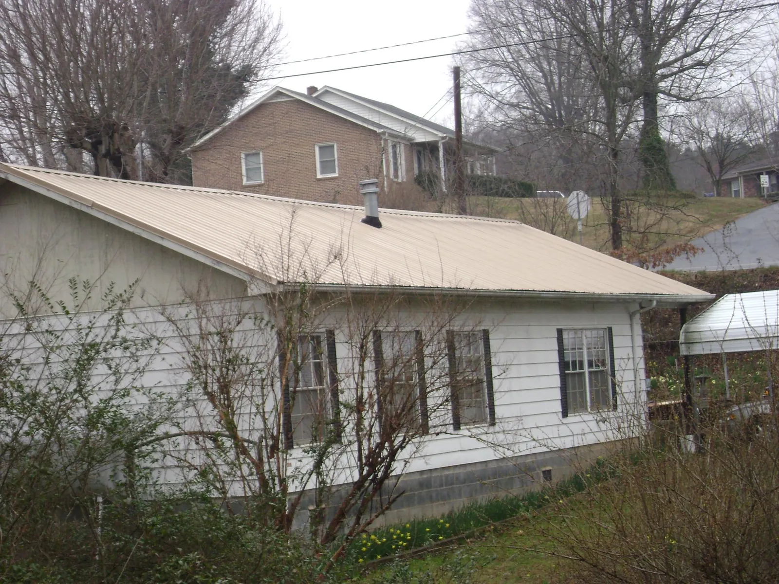 Tan metal roof on a white sided house set into a hillside — Commercial Roofing by Roofing Brothers in Lyman